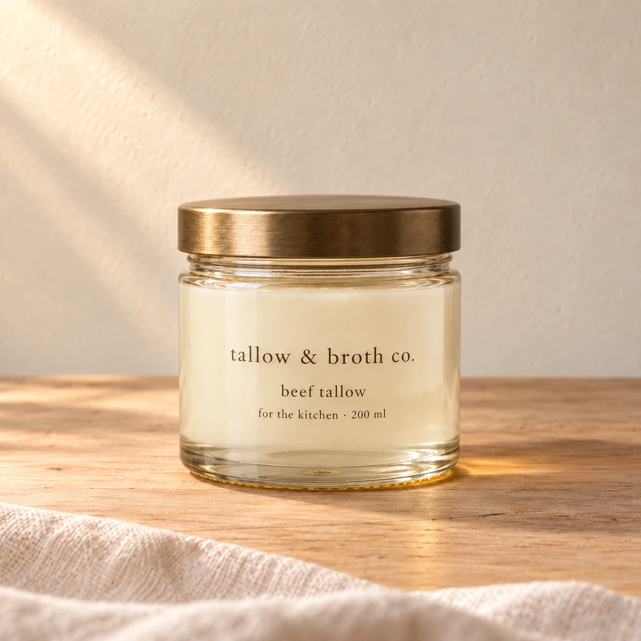 A matching 200 ml glass jar of smooth ivory kitchen beef tallow with a brass lid on warm oak
