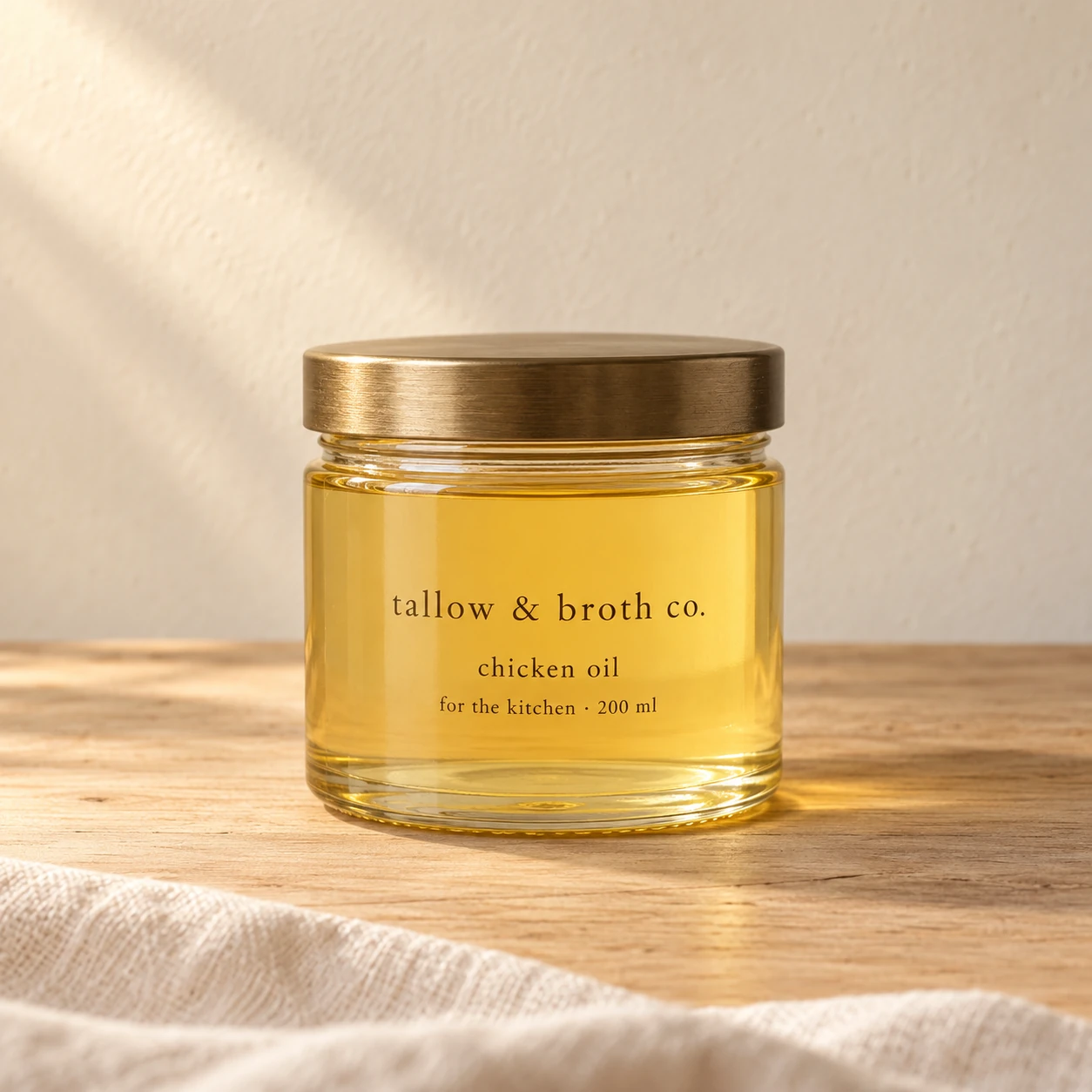 A 200 ml jar of light golden chicken oil with a brass lid on a warm wooden kitchen surface